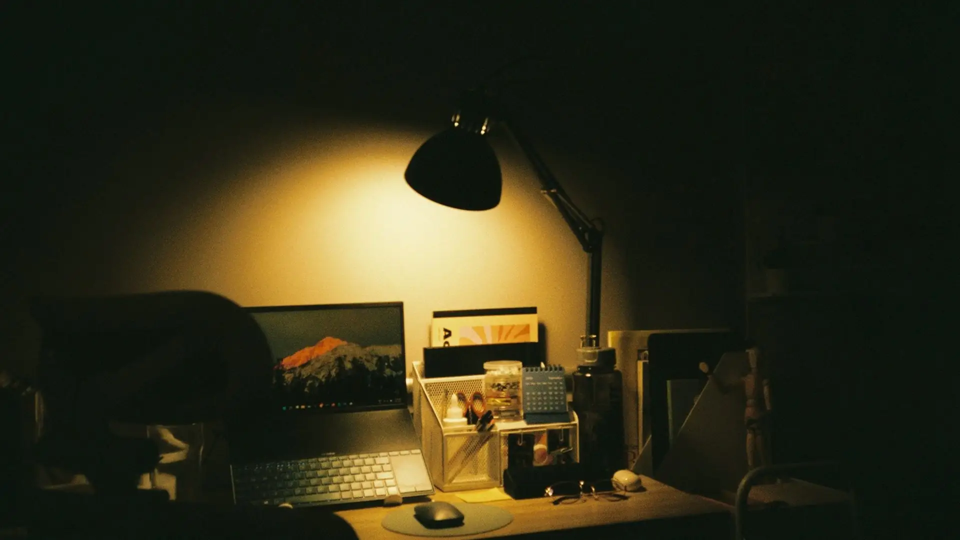 A laptop on a wooden desk under a warm lamp at night